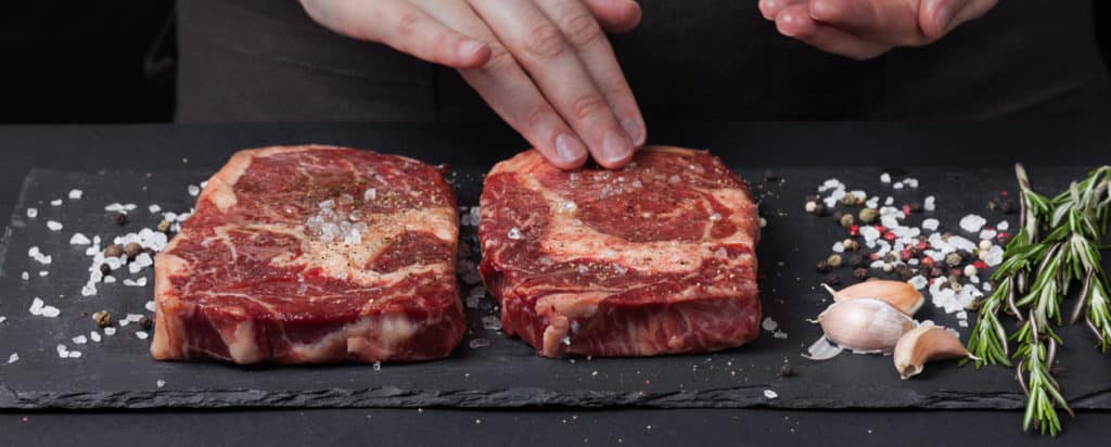 Salzen, Pfeffern und Würzen eines saftigen Stückes Steak. Danach landet das Steak in der Gusspfanne oder auf dem Grill.